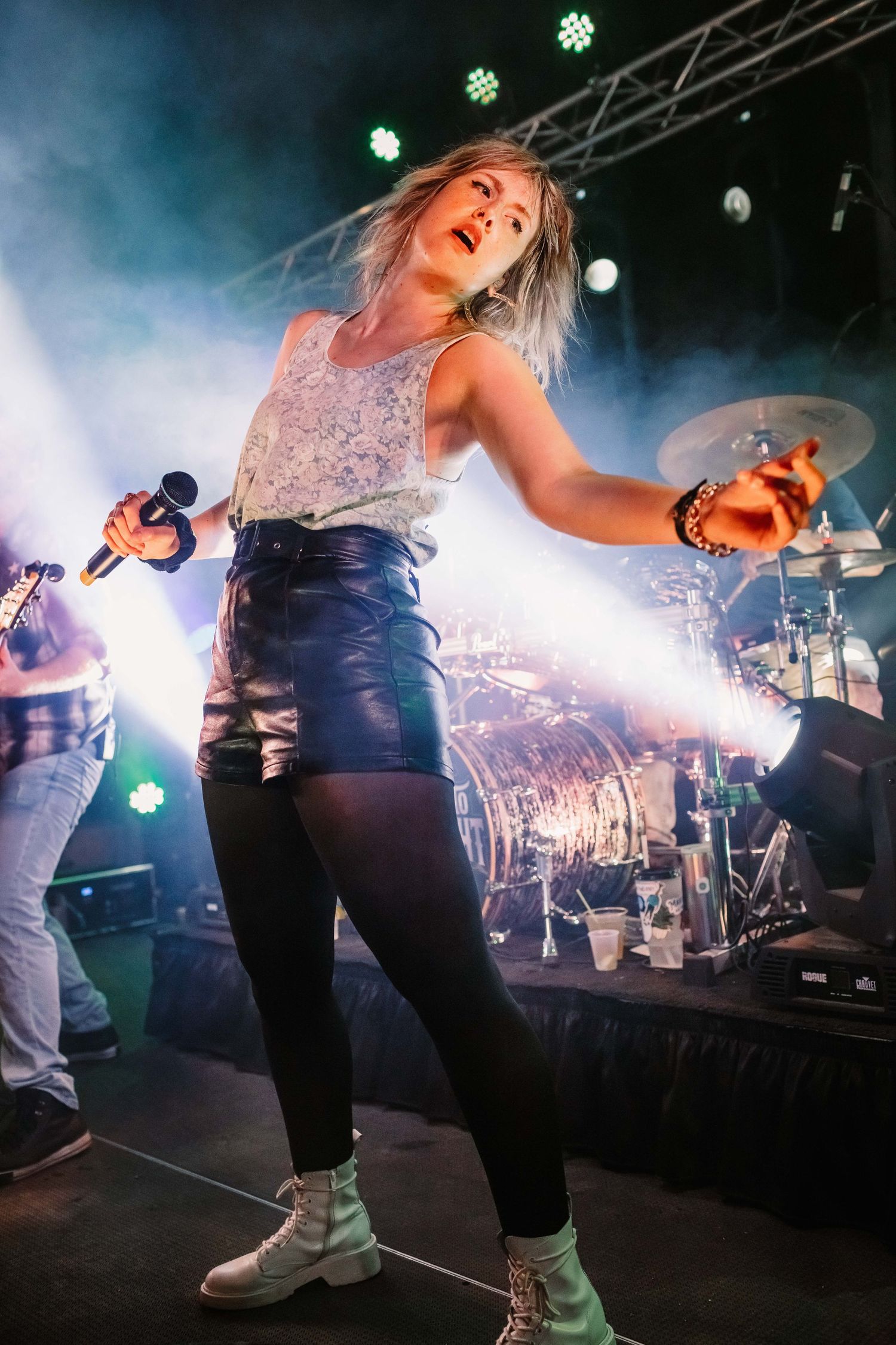 Performer dances energetically on stage wearing a sparkly top and dark pants with dramatic lighting and fog effects.