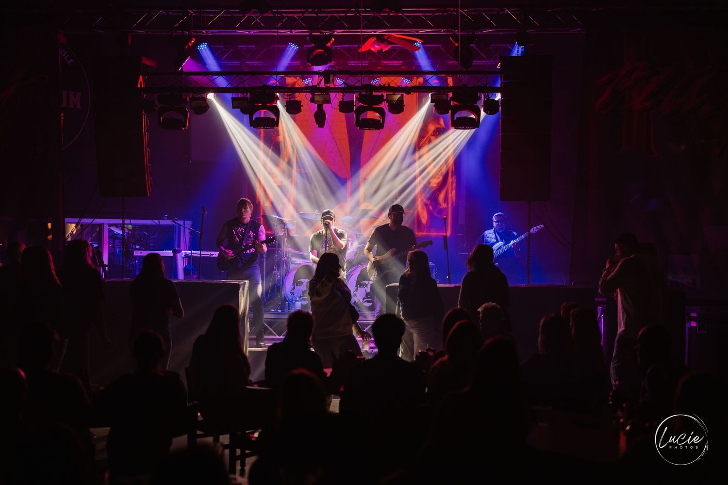 Performers on a dark stage illuminated by purple and white stage lights during a live concert performance.