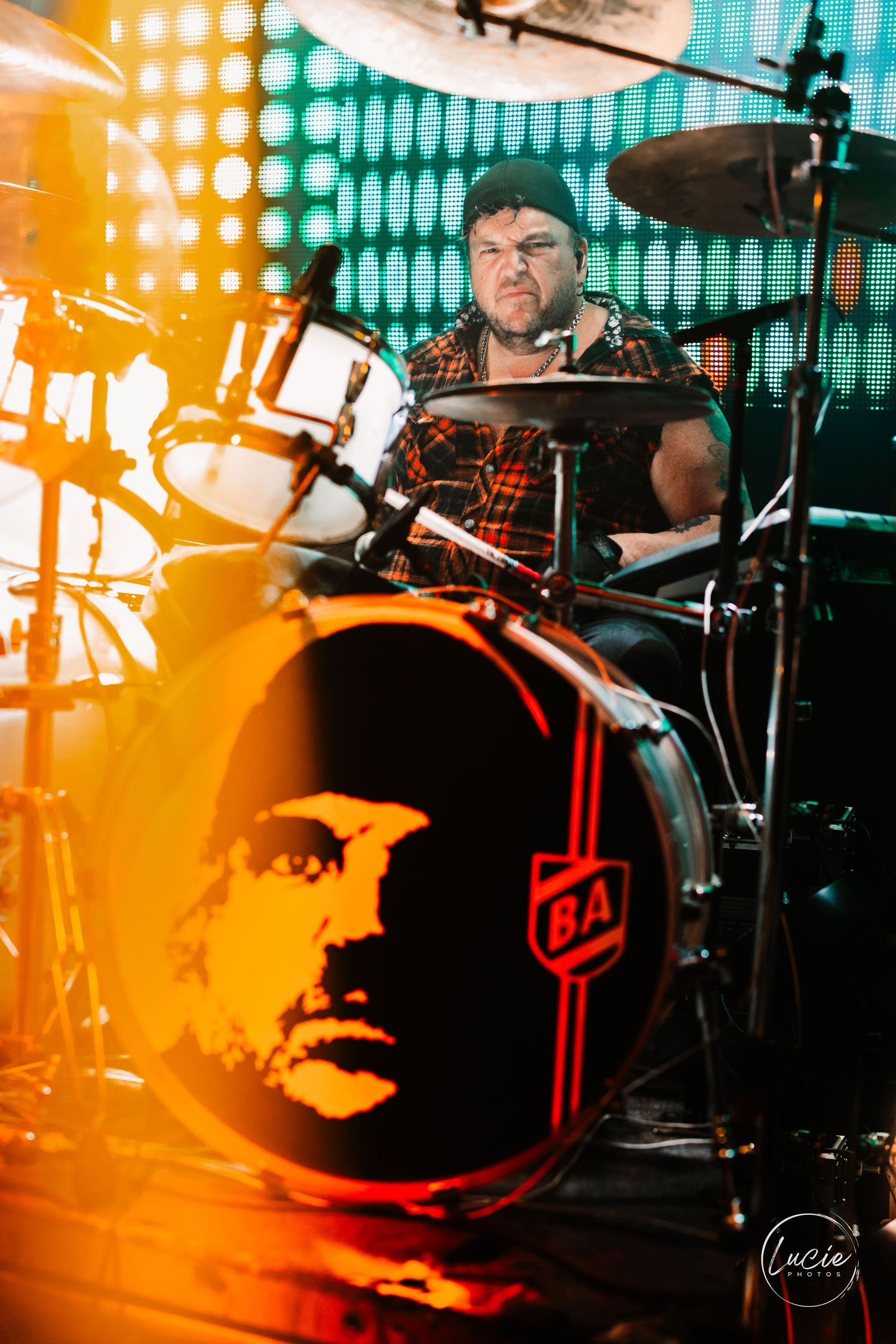 Drummer performs on stage with dramatic orange and blue lighting effects creating an atmospheric concert ambiance.