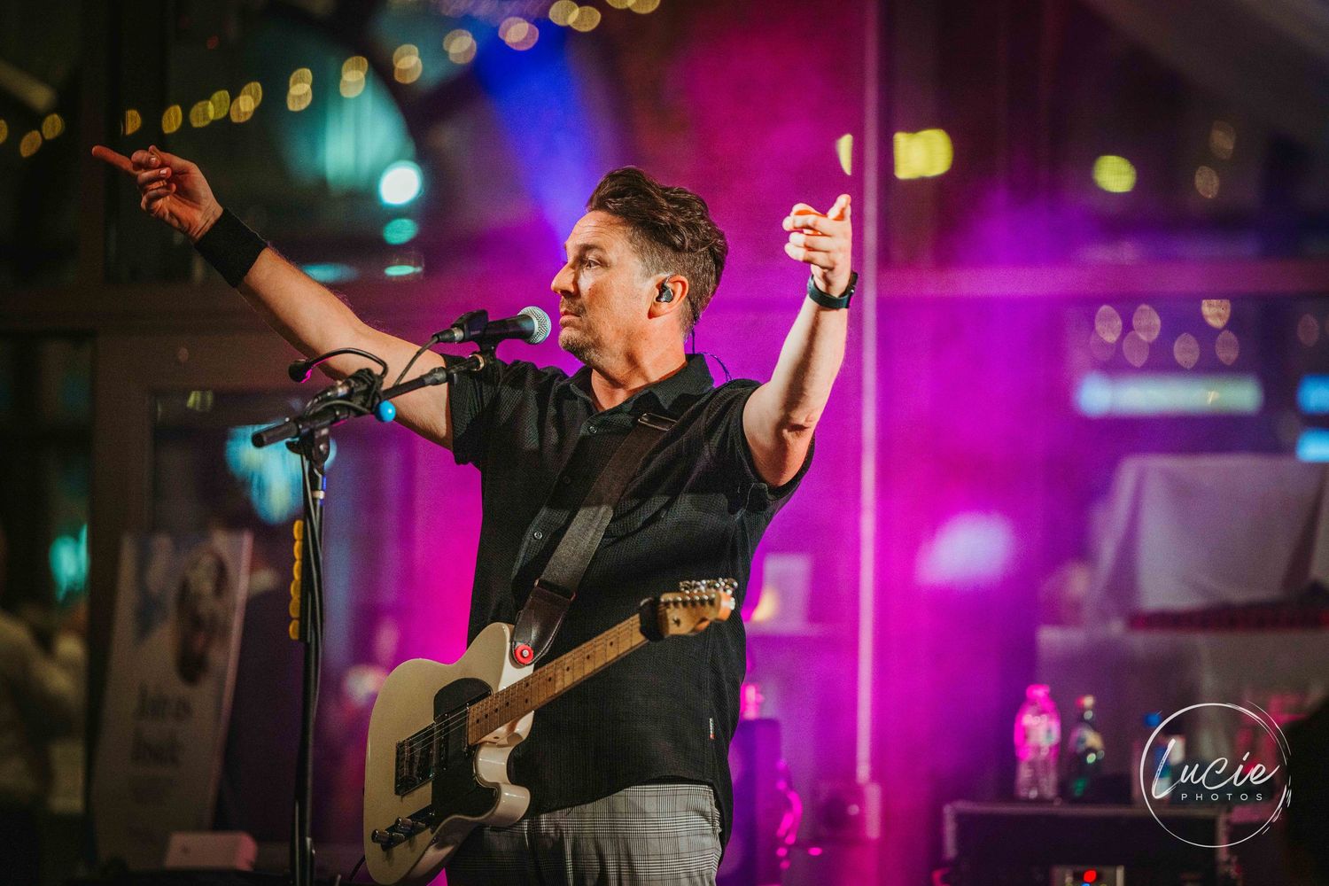 Musicians perform at a concert with vibrant purple and blue stage lighting creating an energetic atmosphere.