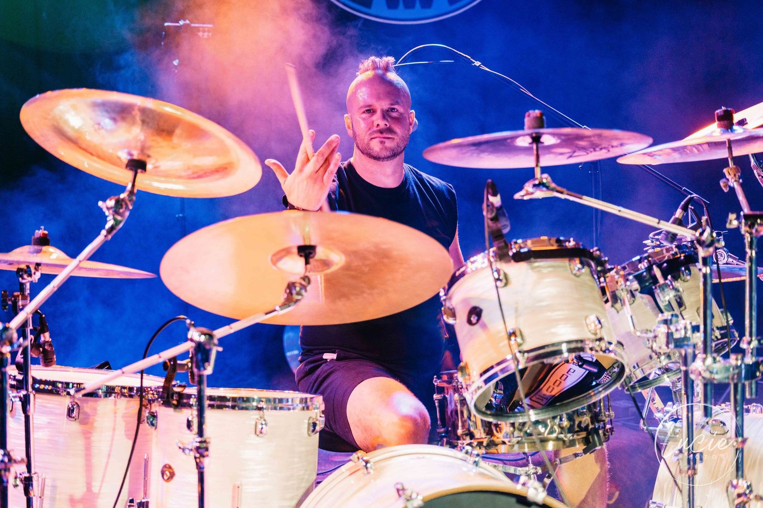 Cropped panoramic concert stage view showing drums with cymbals and lighting equipment during a live performance.