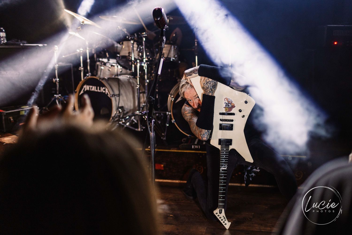 Electric guitarist performing energetic jump on stage with dramatic lighting and smoke effects during live concert performance.