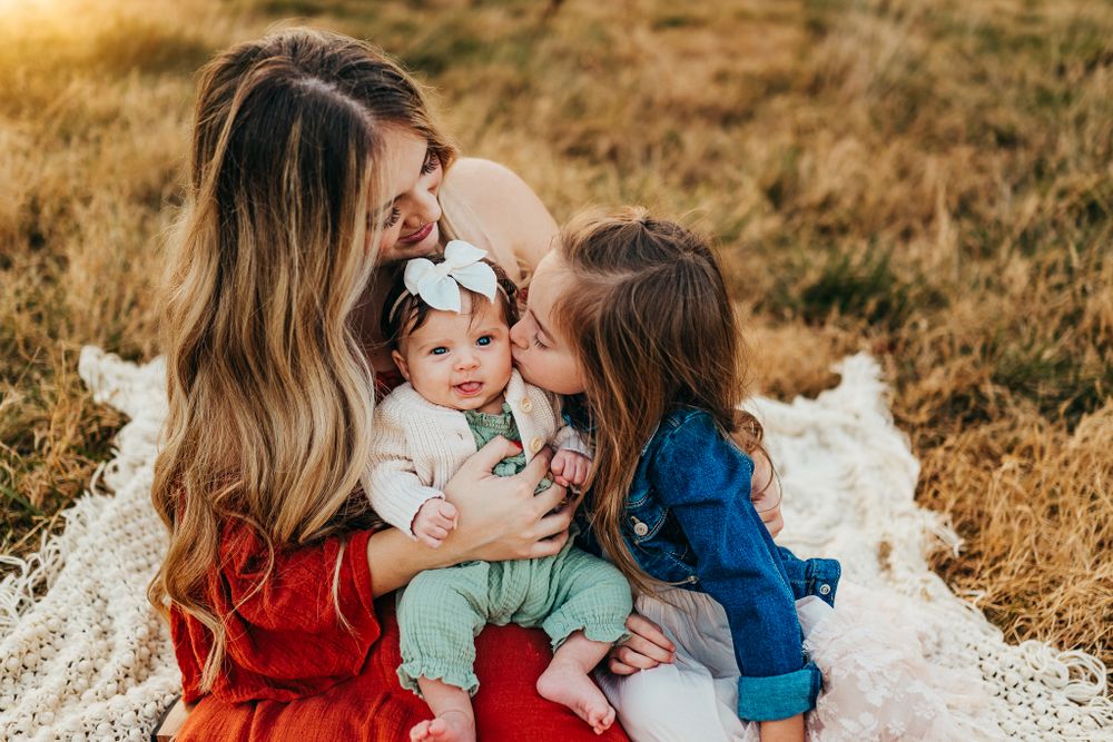 A family shares loving moments together on a white blanket in a golden field.