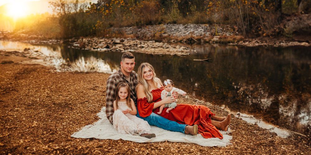 A family relaxes together on a blanket near a serene pond at sunset.