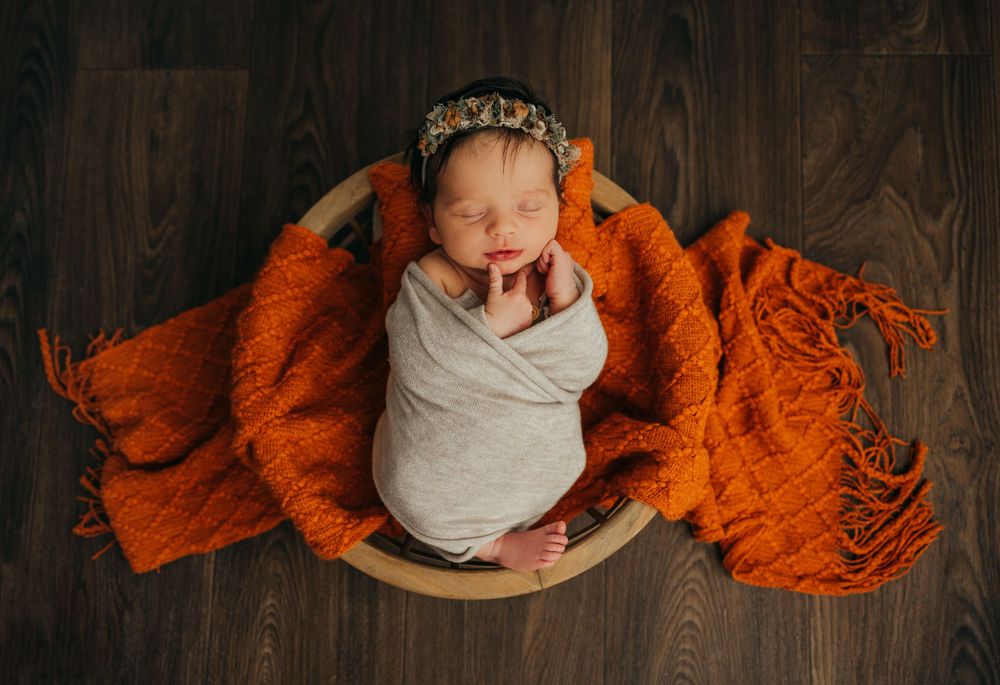 Sleeping newborn wrapped in gray swaddle on wooden bowl with orange blanket backdrop roscoe il newborn photographer