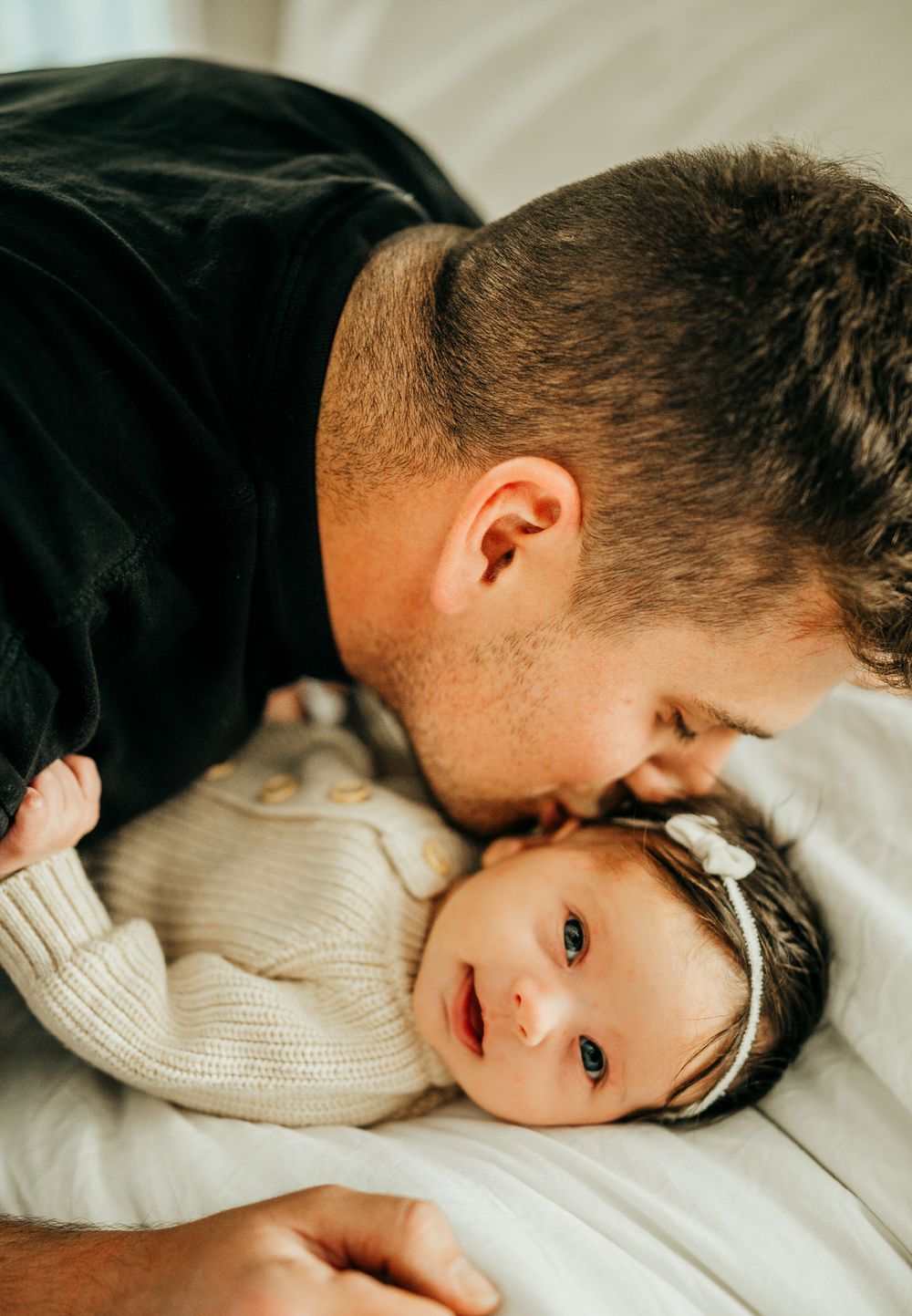A tender moment between parent and baby in white knit clothing on soft bedding.