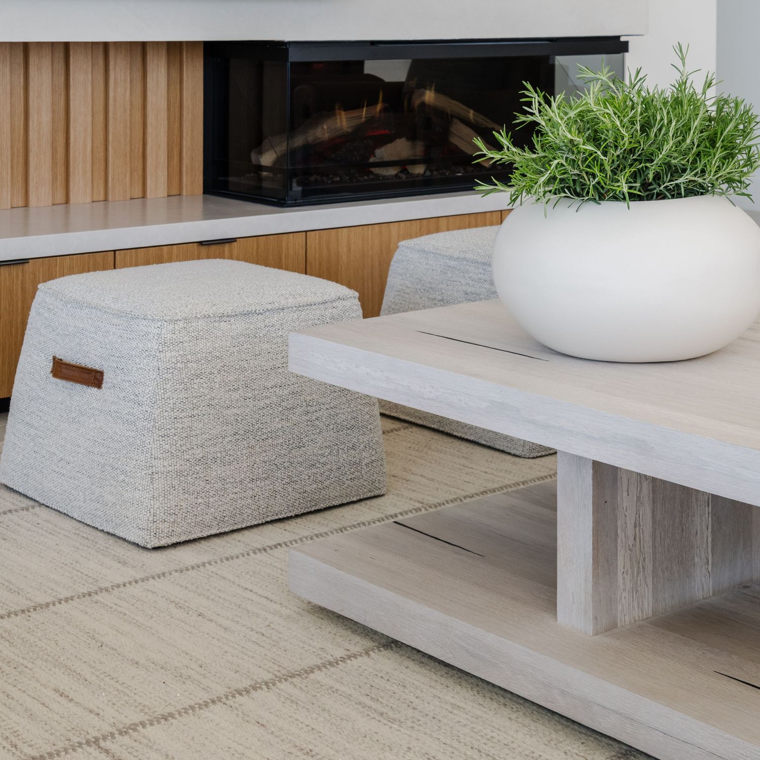 White wood coffee table and gas fireplace with a boucle ottoman near it.