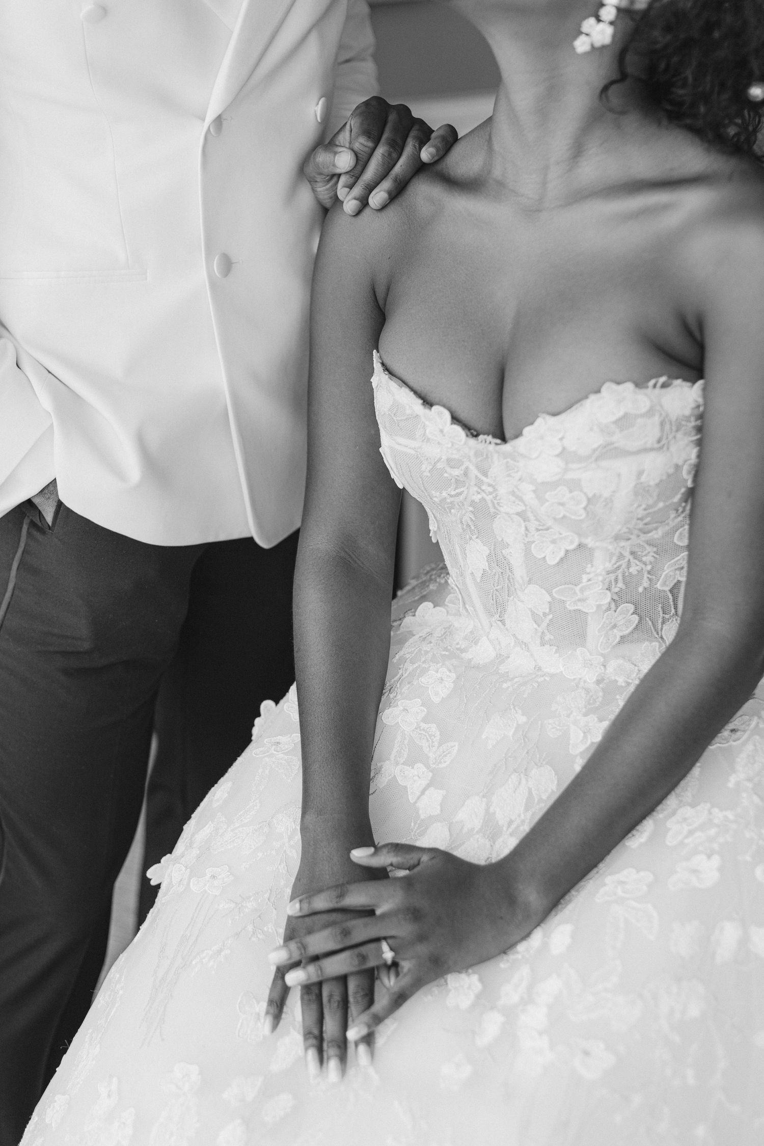 Close-up detail shot of an intricate lace wedding dress bodice and hands clasped together.