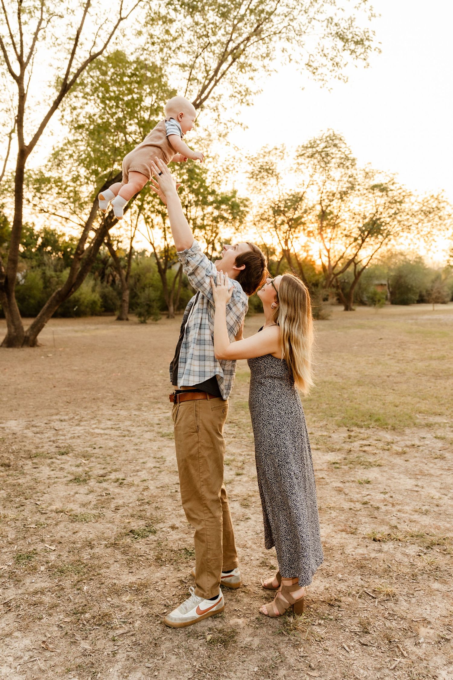 Expecting couple walks hand-in-hand through a golden sunlit field, woman in a white maternity gown.