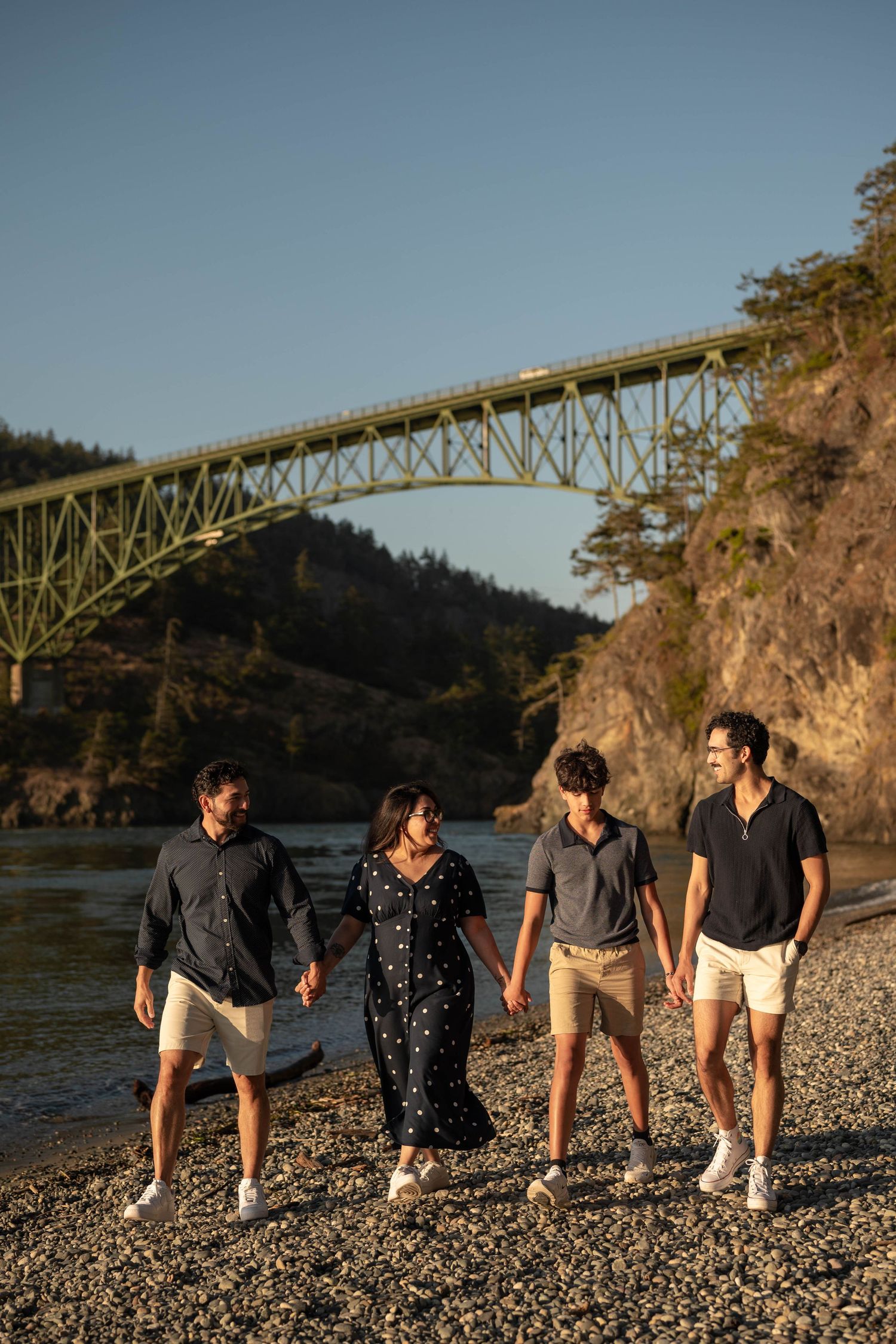 Family photo session along a rocky beach beneath Deception Pass Bridge in Washington during golden hour sunset.