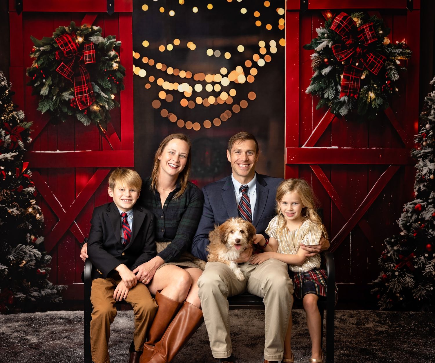 Holiday portrait setup with red barn doors, string lights, and Christmas wreaths.