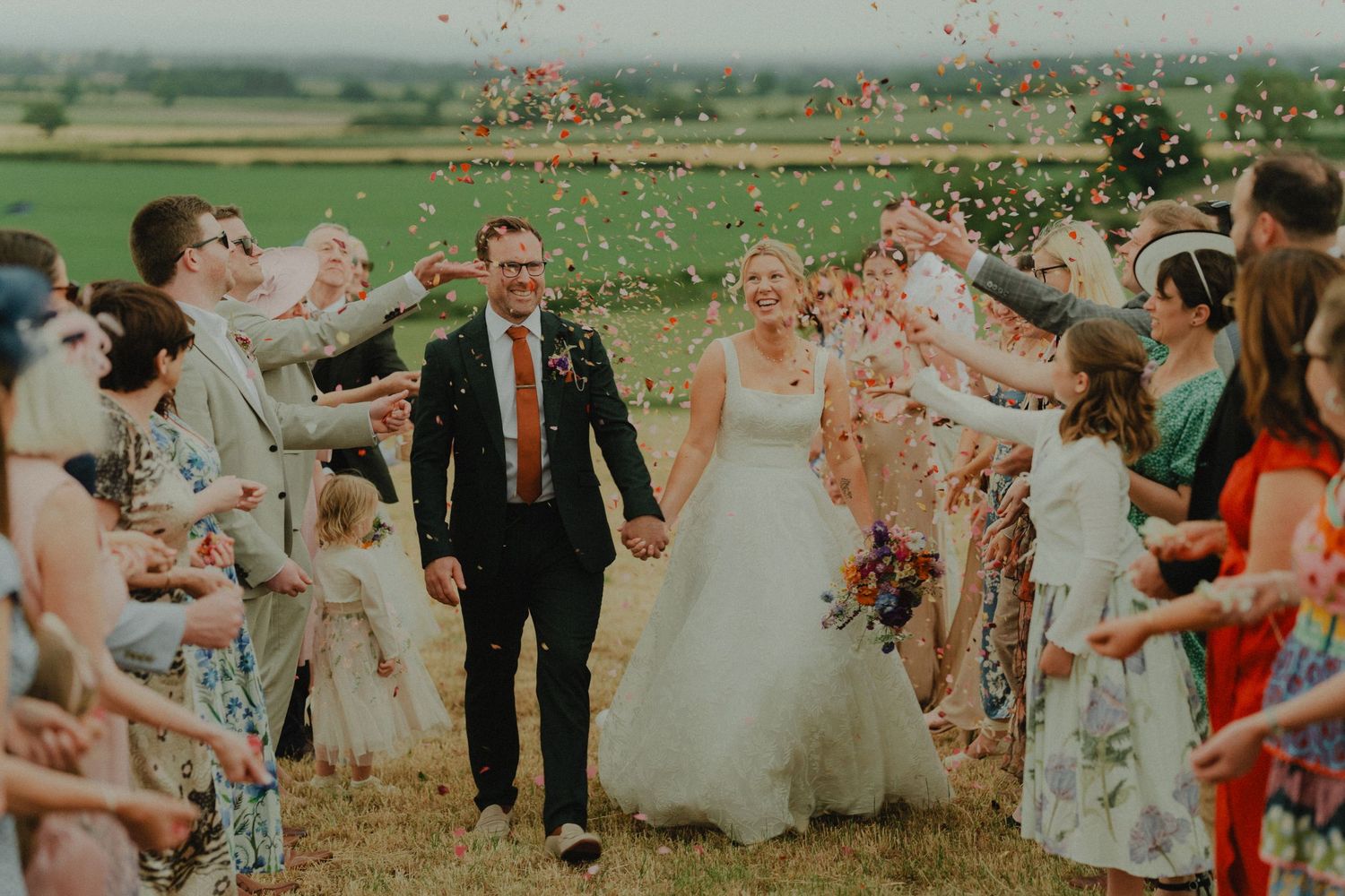 A couple walking away together on a path near a rustic building on their wedding day.