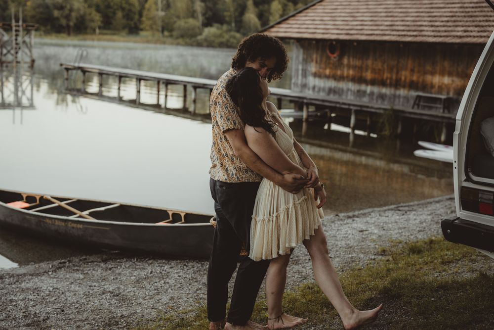 A romantic bride and groom share an intimate moment by a lake during a wedding photoshoot.