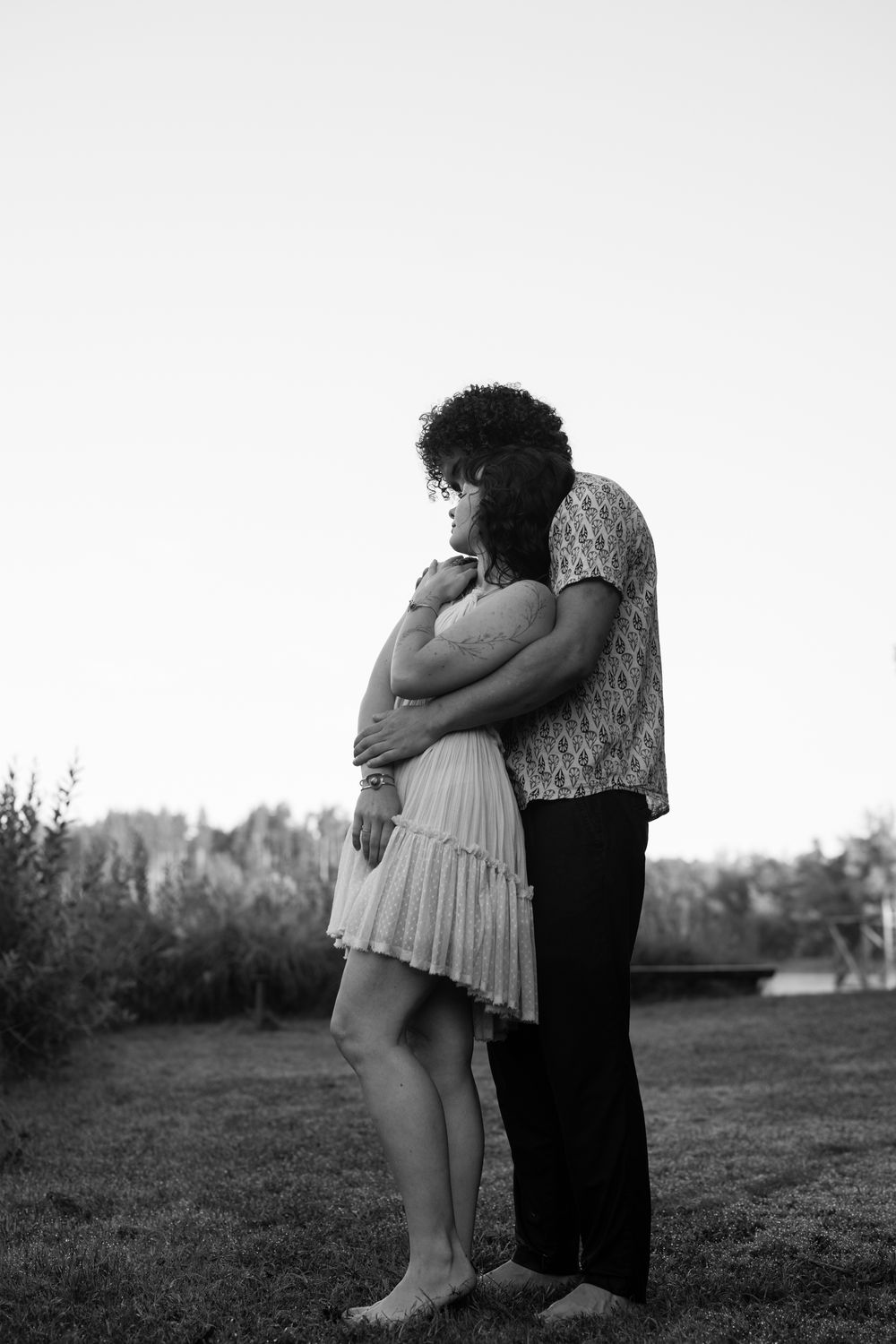 A romantic black and white photo of a couple embracing outdoors in a field with soft lighting and natural backdrop.