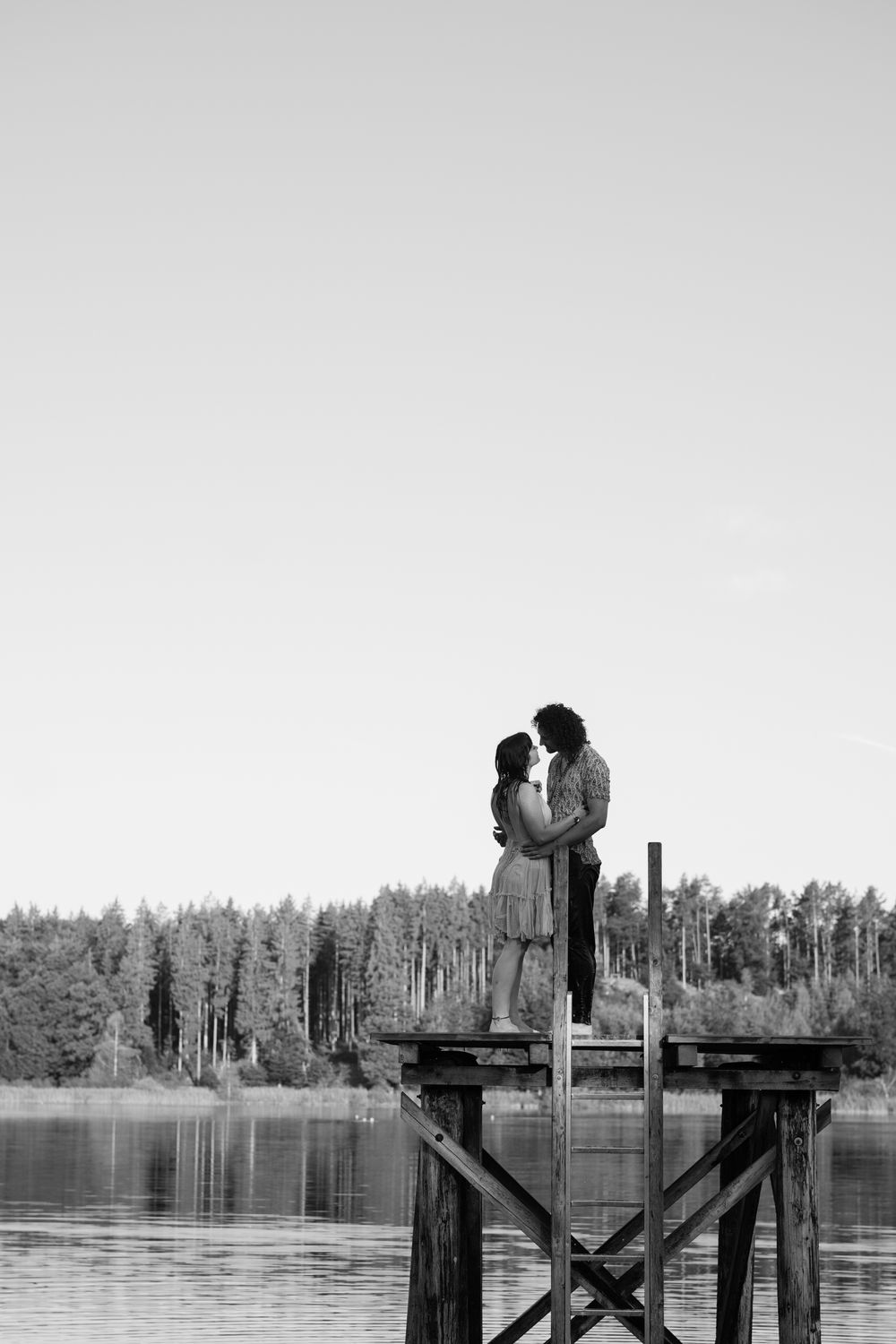 A sequence of black and white photographs shows a silhouetted person sitting on a wooden dock by a calm lake with trees.
