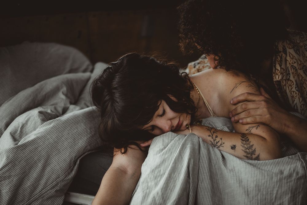 A couple shares an intimate romantic moment together while lying in bed under soft gray bedding.