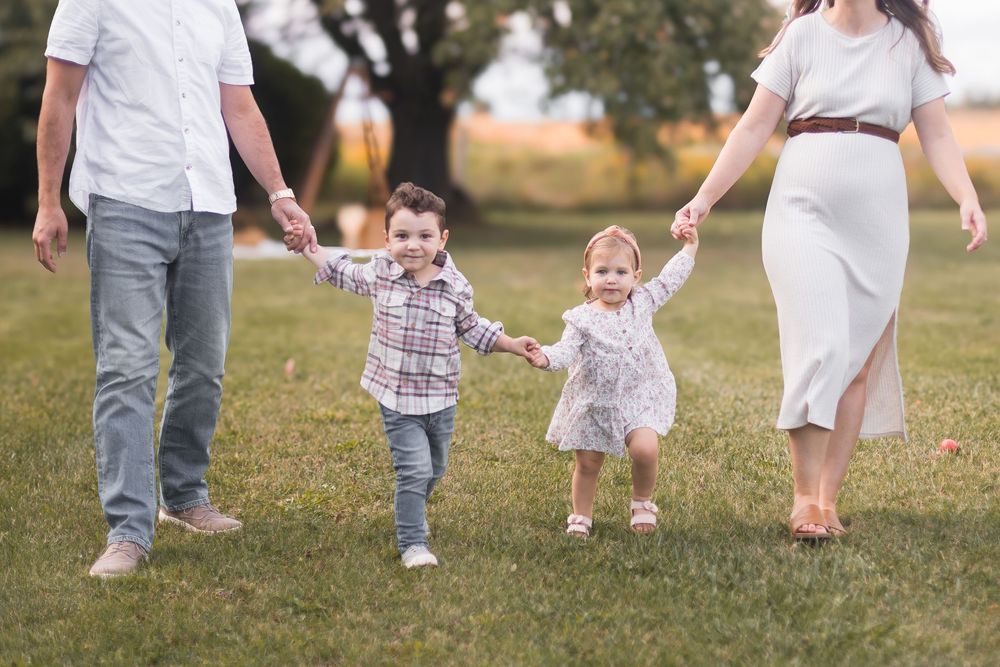Happy family of four holding hands and walking together on a green grassy field outdoors.
