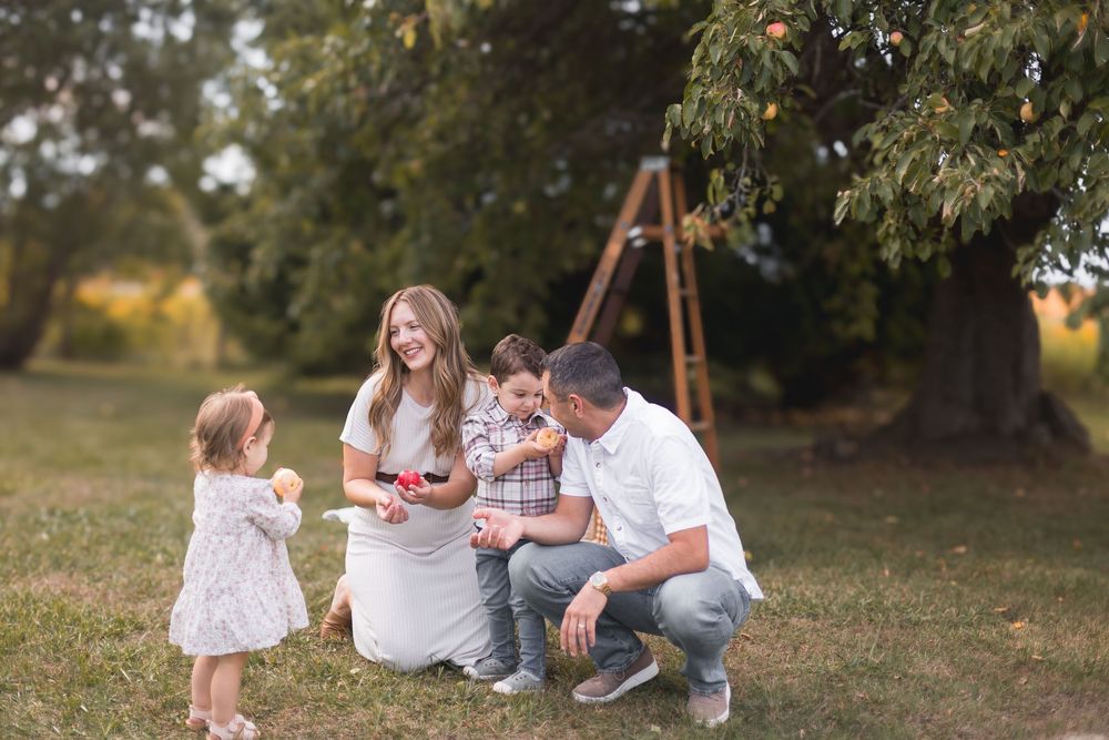 Young family with two children enjoying time together in an orchard during autumn season.