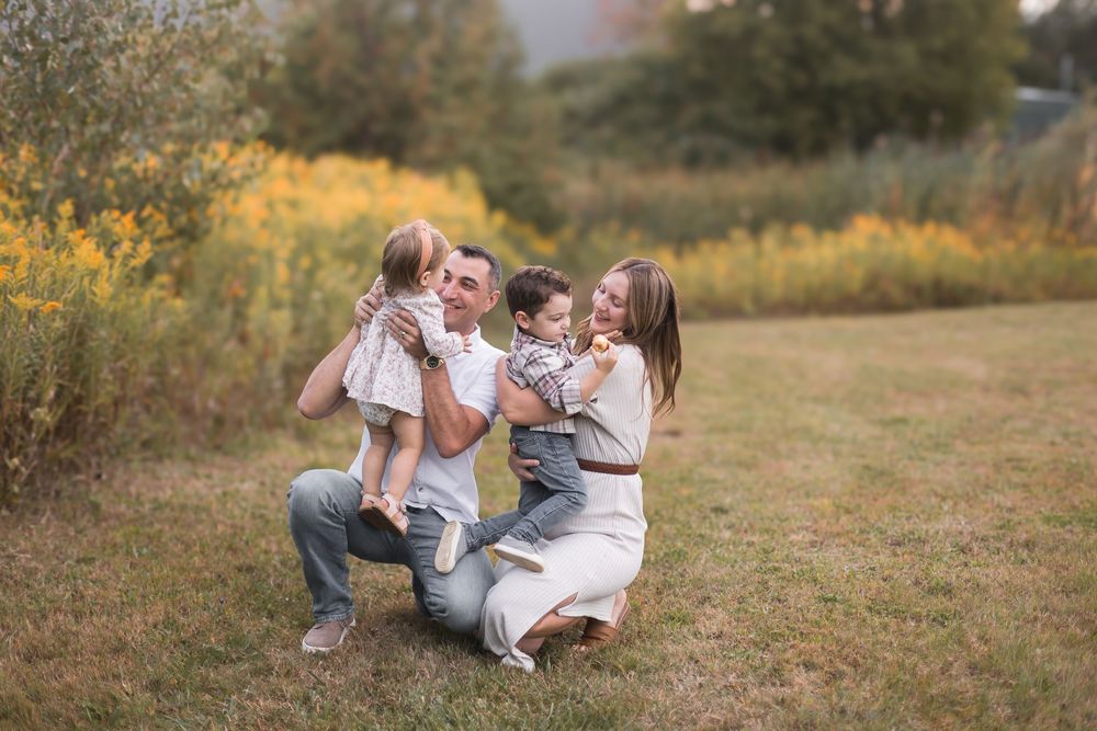Joyful parents lifting two young children in a colorful autumn meadow on a sunny day.