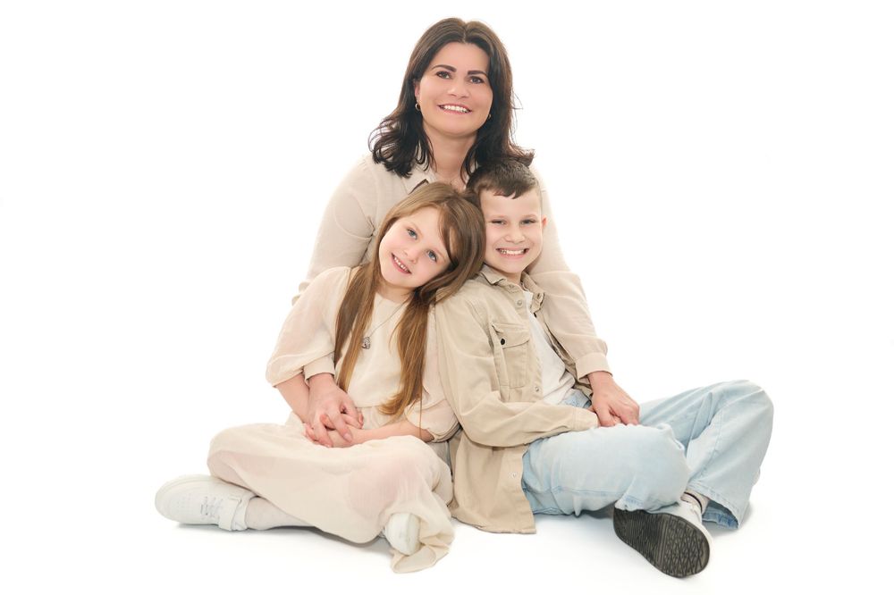 Happy mother sitting with her two children in neutral clothing on white background.
