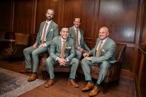 Four groomsmen in sage green suits with brown ties and oxford shoes posing in a wood-paneled room at little river farms in milton georgia.