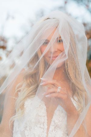 Bride smiling under a sheer veil, wearing a lace wedding dress and diamond ring at montaluce winery in dahlonega georgia