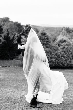 Black and white photo of a groom dipping his bride in a romantic kiss outdoors, her veil flowing gracefully at blue mountain vineyards