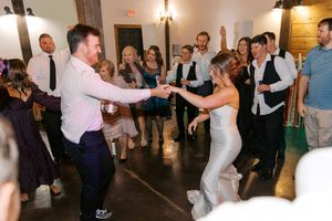 Bride and groom dancing joyfully at wedding reception surrounded by cheering guests in elegant venue at blue mountain vineyards in dahlonega