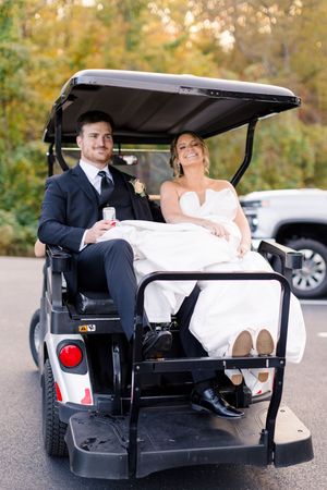 Bride and groom riding a golf cart on their wedding day, smiling joyfully, surrounded by autumn foliage at blue mountain vineyards