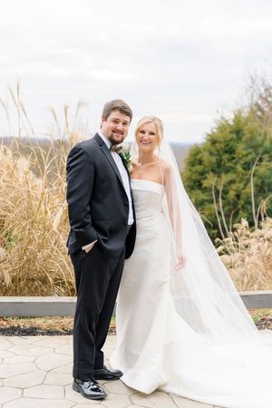 Bride in white strapless gown with veil and groom in black tuxedo pose outdoors with autumn grasses backdrop at wolf mountain vineyards.