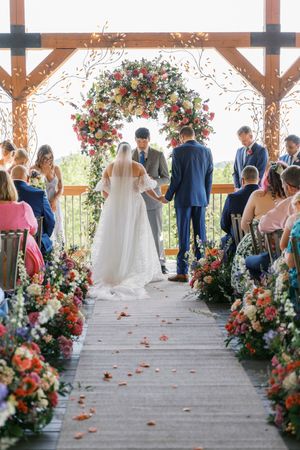 Bride and groom exchange vows under a floral arch at ceremony with colorful flowers lining the aisle at wolf mountain vineyards