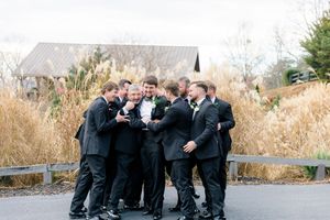 Groom and groomsmen laughing together outdoors at a wedding venue with tall golden grasses in the background at wolf mountain vineyards.