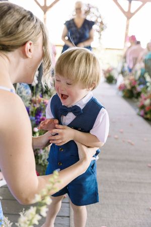 Adorable toddler boy in blue vest and bow tie laughing joyfully at a wedding ceremony at wolf mountain vineyards