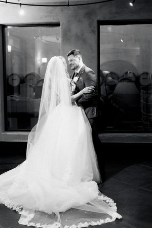 Black and white photo of a smiling groom embracing his bride in a flowing wedding gown during first look at montaluce winery in dahlonega