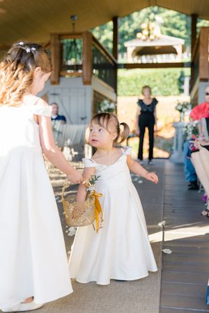 flower girls walk down the wedding aisle, one holding a wicker basket with yellow ribbon at wolf mountain vineyards in dahlonega georgia