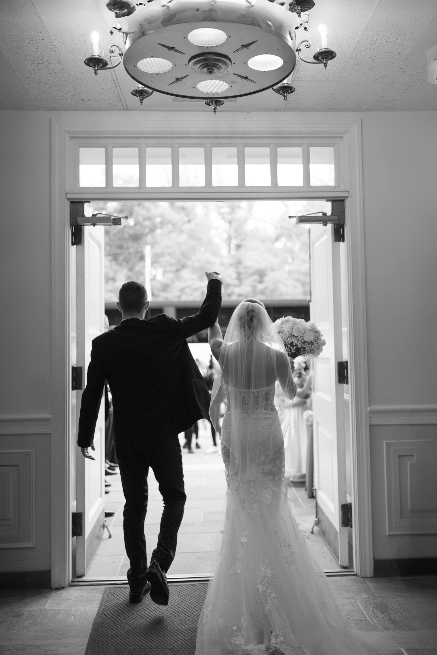 Black and white photo of newlyweds raising hands while exiting through church doors after ceremony.