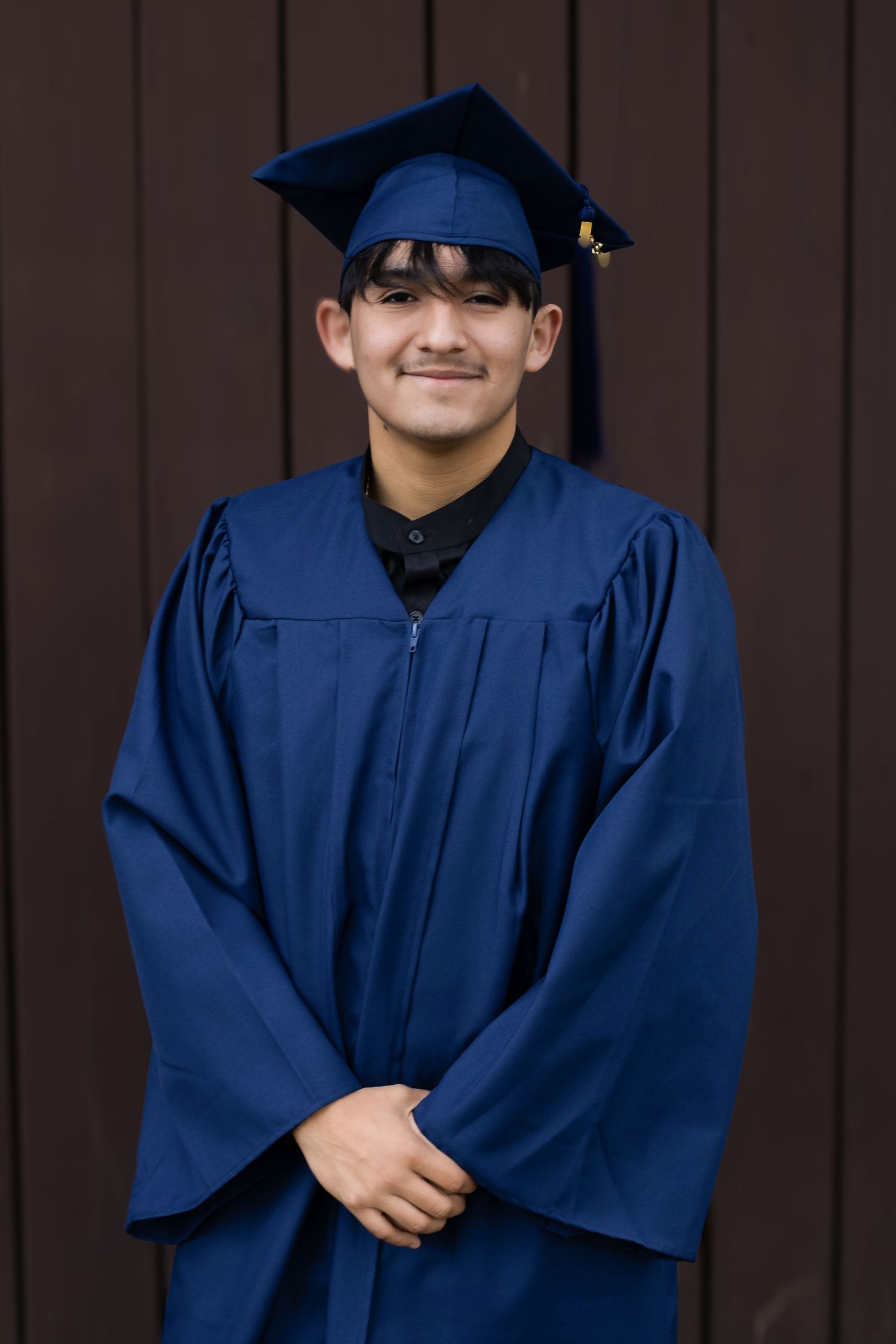 Graduate poses in navy blue cap and gown against brown background.