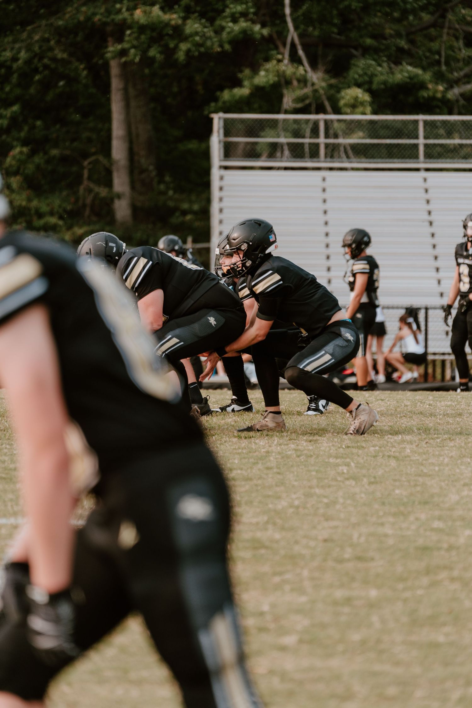 Football players in black uniforms line up in formation during practice on a grassy field.