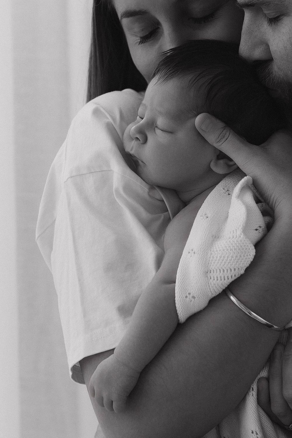 A sleeping newborn baby wrapped in a cozy white knit blanket.