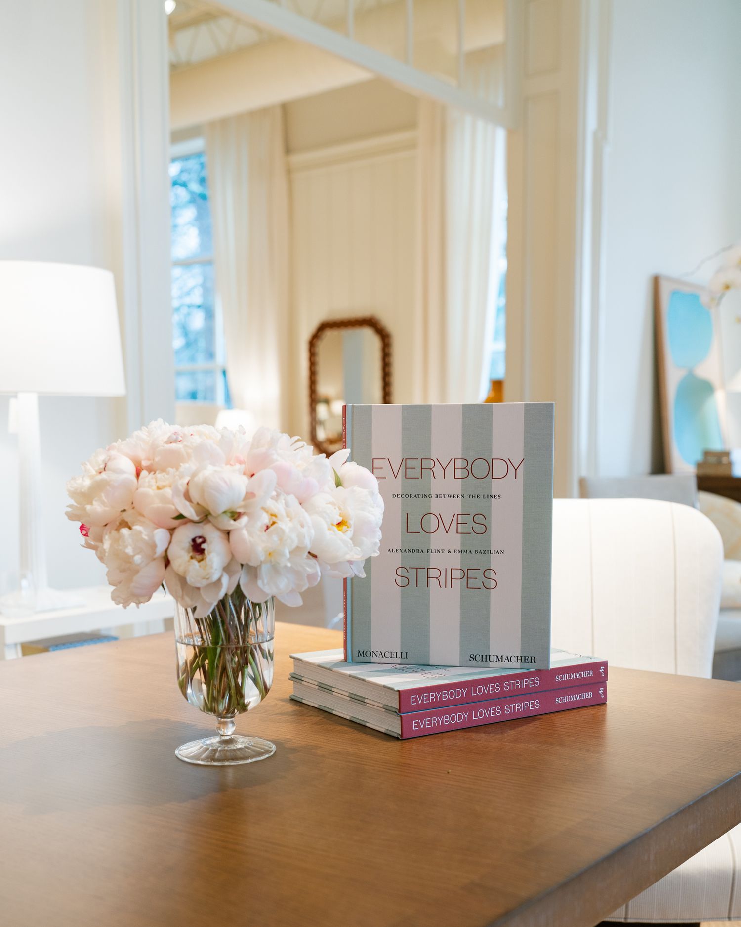 Pink peonies beside striped book on wooden table in bright room.