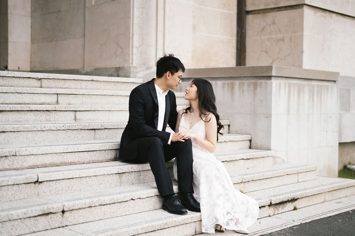 Intimate wedding moment captured on elegant white marble steps of a grand building.