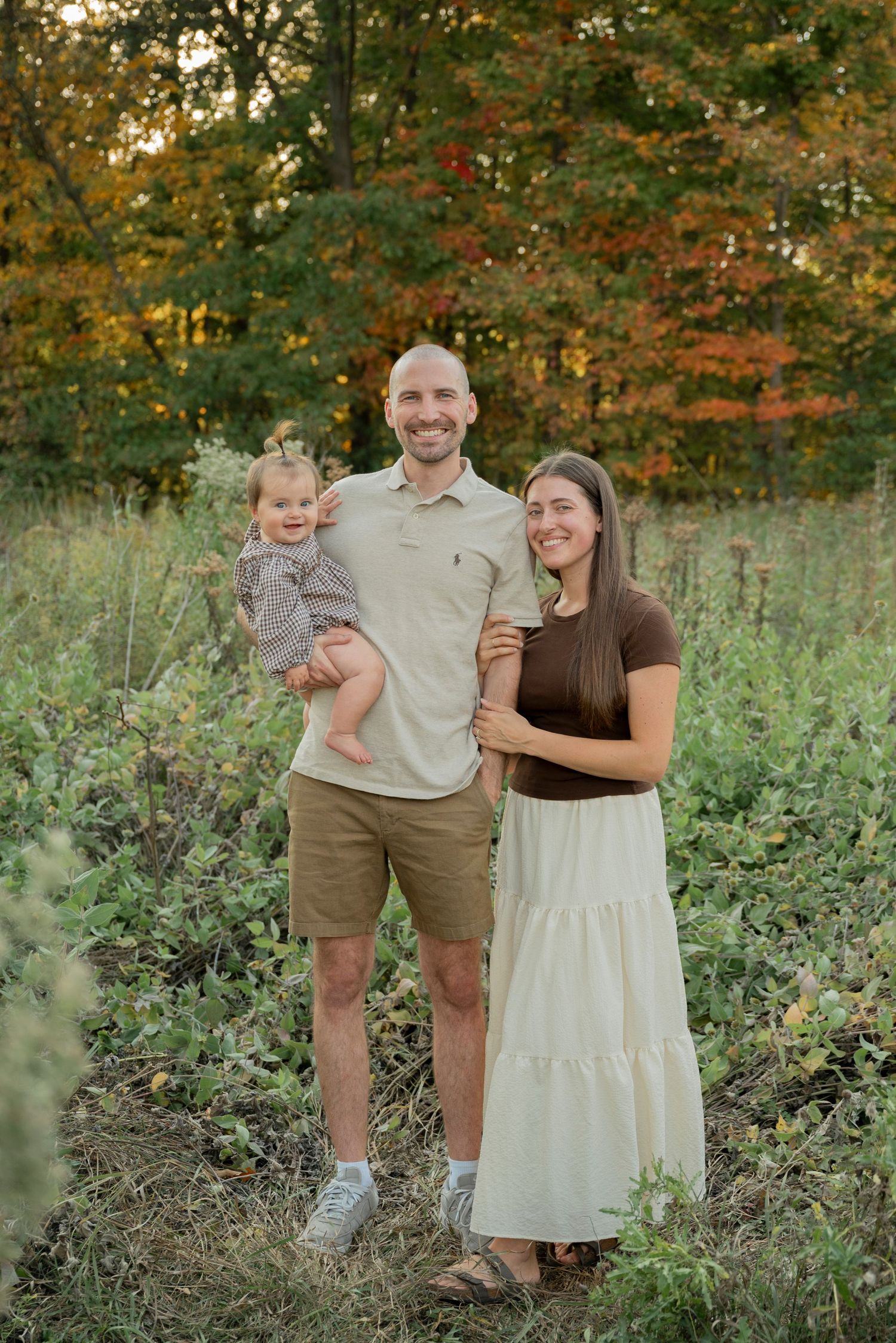 Three people pose together outdoors in a natural setting with autumn foliage in the background.