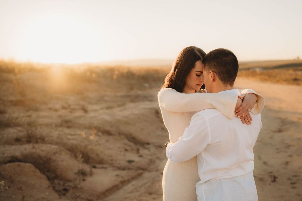 Couple embracing romantically at golden sunset in a sandy desert landscape.