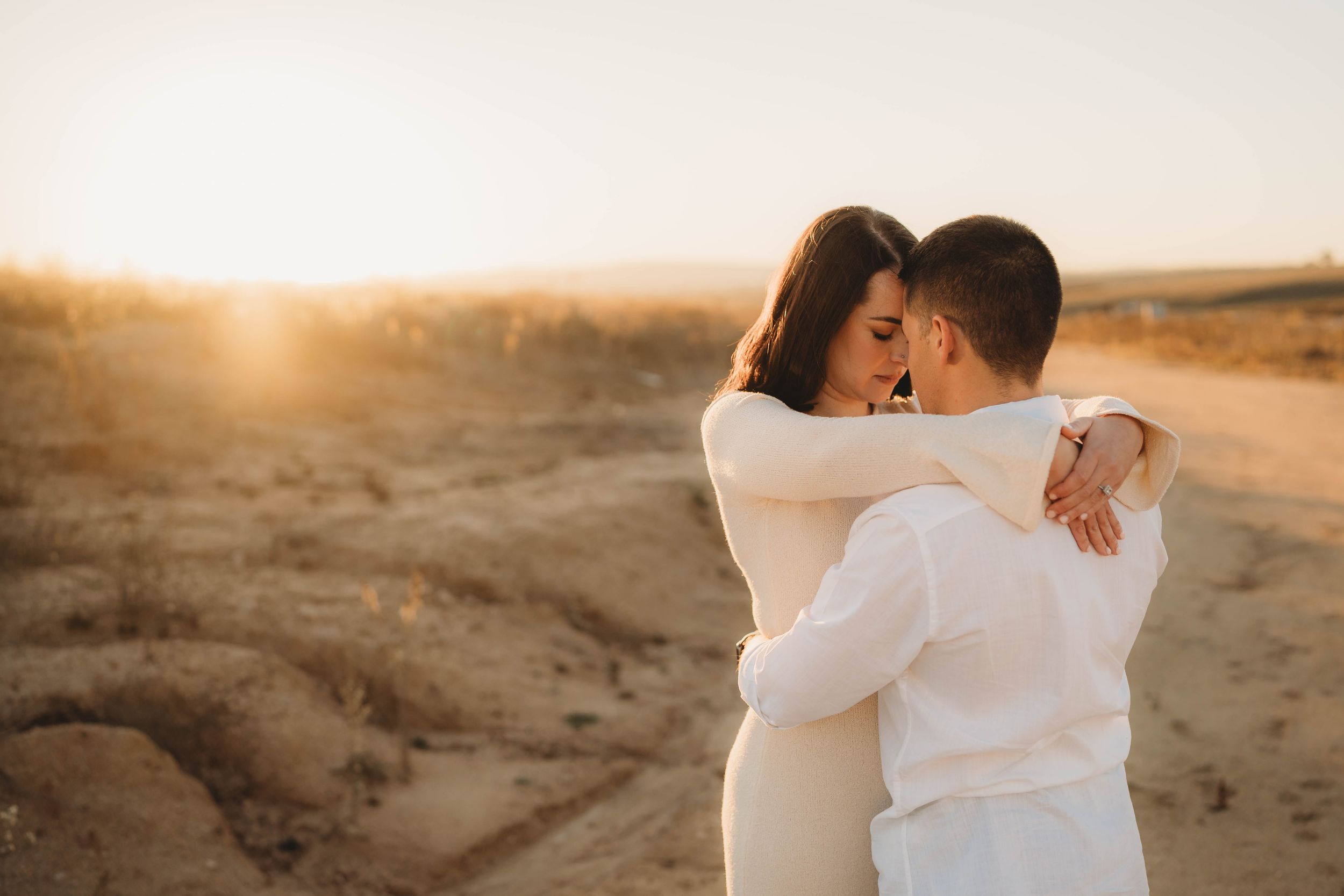 Couple embracing romantically at golden sunset in a sandy desert landscape.