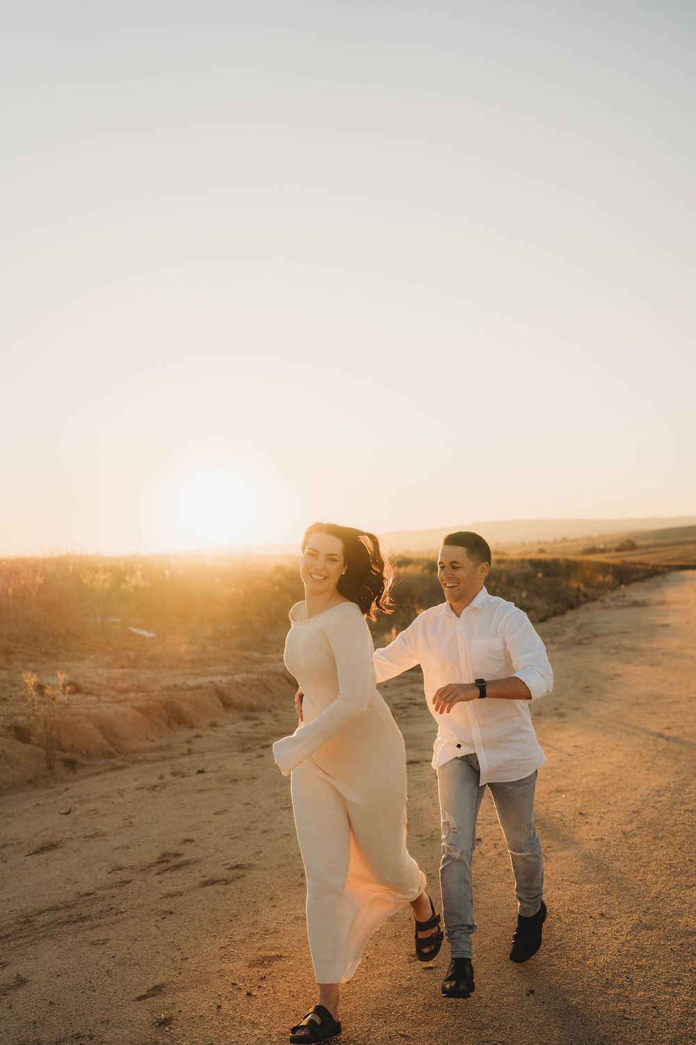 Happy couple walking hand in hand along a dusty road during a warm golden sunset.
