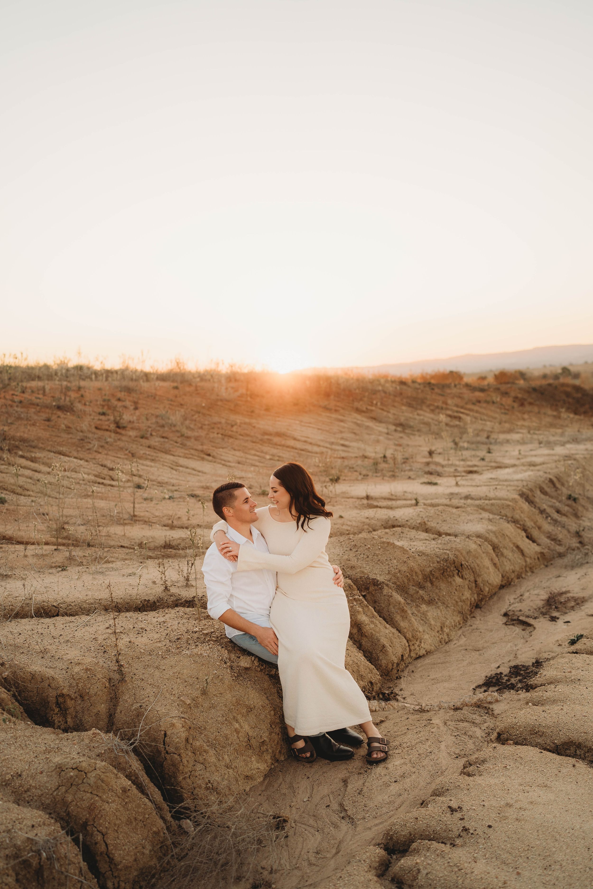 Romantic couple sitting together on sandy terrain sharing a tender moment at sunset.