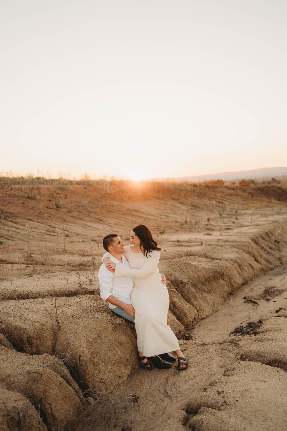 Romantic couple sitting together on sandy terrain sharing a tender moment at sunset.