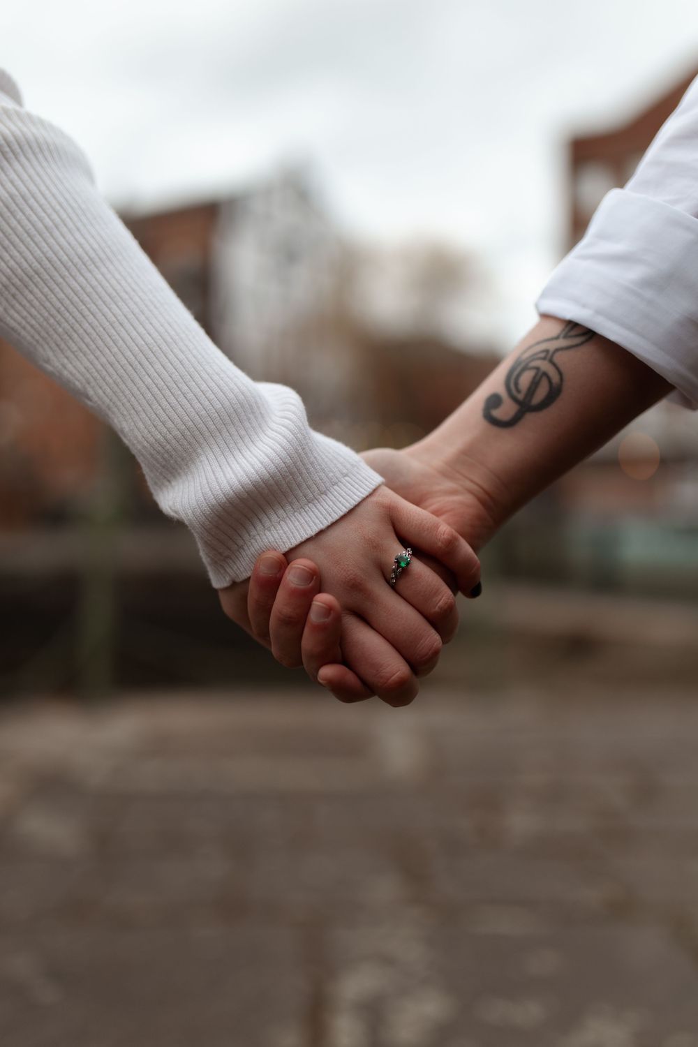 Close-up of two people holding hands with visible tattoo and ring against blurred background. Leeds City Centre Pre Wedding Session.