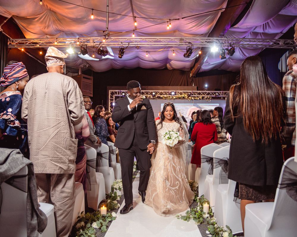 Bride and groom walking down the aisle together at an elegant tented wedding ceremony with string lights.