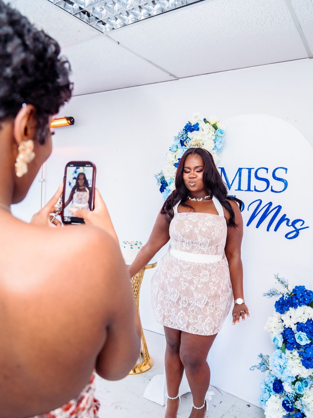 Bride in white lace dress posing for a photo in front of a Miss to Mrs wedding backdrop.